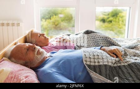 Senior Coupe schläft in der Morgensonne im Bett Stockfoto