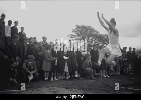 1952, historisch, ein älterer männlicher Student, der den Weitsprung machte, beobachtet von einer Gruppe von Erwachsenen und Schulkindern, Schottland, Großbritannien. Stockfoto
