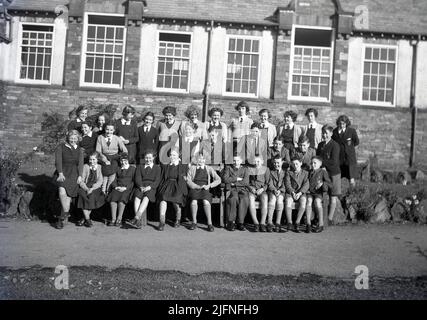 1951, historisch, eine große Klasse von aufgeregten Schulkindern in ihrer Uniform, die vor ihrem Schulgebäude sitzen und für ein Gruppenfoto stehen, England, Großbritannien. Stockfoto