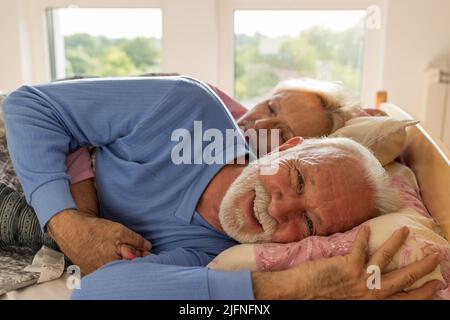 Älterer Mann, der morgens wach im Bett lag, während seine Frau noch in Umarmung schlief Stockfoto