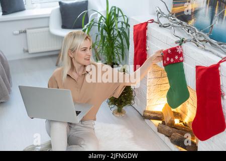 Frau, die einen Laptop benutzt und jemanden während eines Videoanrufs am Weihnachtsabend zu Hause begrüßt. Junge schöne Frau feiert Neujahr oder Cristmass AT Stockfoto