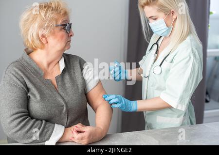 Allgemeinmediziner impft alten Patienten in der Klinik mit Kopierplatz. Arzt, der einer älteren Frau im Krankenhaus eine Injektion verabreicht. Krankenschwester hält Spritze Stockfoto