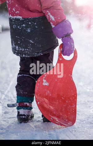 Das Mädchen hält einen roten Schlitten in den Händen, um den Hügel zu reiten. Schlittenfahren. Aktivitäten für Kinder und Jugendliche. Winterunterhaltung und Sport. Stockfoto