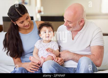 Junge glücklich interracial Paar Bonding mit ihrem adoptierten Baby zu Hause. Kleines Mädchen lächelt, nachdem es von einem kaukasischen Mann und gemischter Rasse adoptiert wurde Stockfoto