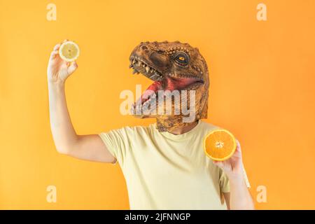 Frau trägt surreale Tierkopfmaske mit frischen Zitronen- und Orangenscheiben, isoliert auf orangefarbenem Hintergrund mit Kopierraum Stockfoto