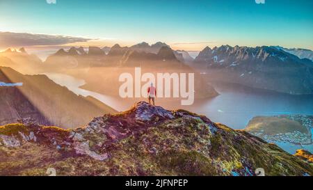 Wanderer mit Blick auf die herrlichen Berge, die von der Mitternachtssonne beleuchtet werden, in Reinebringen, Lofoten, Norwegen Stockfoto