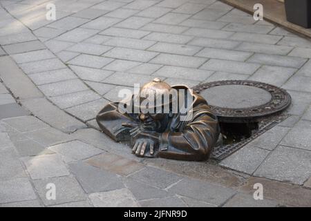 Skurrile Bronzestatue (1997) eines Kanalarbeiters (Čumil, der Wächter), der aus einem Schachtloch im Zentrum von Bratislava, Slowakei, hervorging. Ist er ein piepende tom? Stockfoto