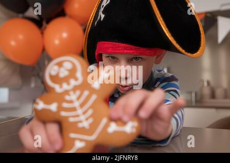 Ein als Pirat gekleideter Junge isst an Halloween Skelett-Lebkuchen und spielt mit Keksen Stockfoto