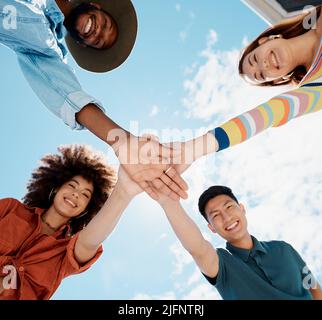 Blick aus dem niedrigen Winkel auf eine Gruppe von Menschen, die zusammengekauert mit in der Mitte angehauerten Händen stehen. Afroamerikanische Frau mit einem Afro. Tausendjährig Stockfoto