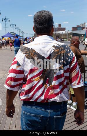 Coney Island, NY, USA. 4.. Juli 2022. Der Strand und die Promenade von Coney Island sind voller Menschen, als New York den 4. Juli feiert. Ein Mann auf dem Boardwalk trägt ein Hemd mit einem Adler, der auf einer amerikanischen Flagge aufgesetzt ist. Quelle: Ed Lefkowicz/Alamy Live News Stockfoto