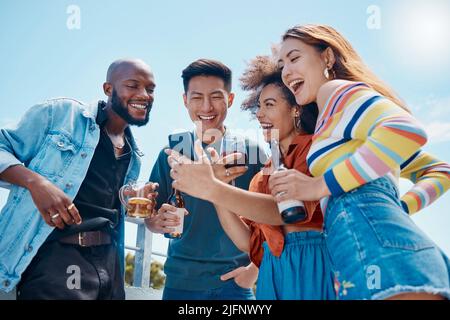 Eine Gruppe verschiedener junger, fröhlicher Freunde, die draußen zusammen stehen und ein Handy für Selfies und Social Media nutzen. Lächelnde Männer und Frauen Stockfoto