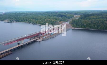 Luftaufnahme einer Brückenkonstruktion. Clip. Fliegen über einen breiten Fluss, eine Brücke und einen grünen Wald. Stockfoto