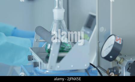 Schüttler zum Mischen von Lösungen wird die flüssige Substanz von einer Maschine in einem Labor gemischt. Aktion. Professioneller Schüttler mit Kolbenbewegung. Stockfoto