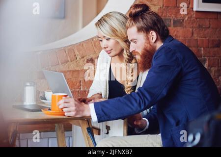 Junge gemischte Rennen verschiedene Kollegen treffen sich in einem Café, während sie als Team an einem Projekt arbeiten. Multirassische Arbeiter, die während des Brainstorming einen Laptop verwenden Stockfoto