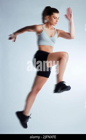 Shes hat echte Geschwindigkeit. Ganzkörperaufnahme einer attraktiven jungen Sportlerin, die vor grauem Hintergrund im Studio posiert. Stockfoto