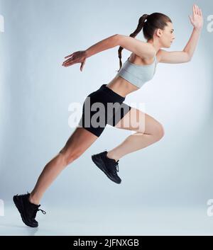 Und shes ab. Ganzkörperaufnahme einer attraktiven jungen Sportlerin, die vor grauem Hintergrund im Studio posiert. Stockfoto