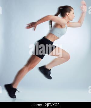 Shes kurz vor dem Start. Ganzkörperaufnahme einer attraktiven jungen Sportlerin, die vor grauem Hintergrund im Studio posiert. Stockfoto