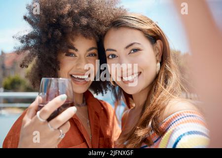 Zwei schöne junge Frauen mit gemischter Rasse stehen zusammen und machen ein Selfie, während sie sich draußen verbinden. afroamerikanerin mit einem Afro, der mit ihr Wein trinkt Stockfoto