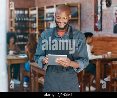 Ein junger afroamerikanischer Geschäftsmann, der eine Schürze trägt und in einem Einzelhandelsgeschäft mit einem digitalen Tablet arbeitet. Porträt eines lächelnden Inhabers eines kleinen Unternehmens Stockfoto