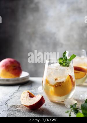 Kalte Getränke im Sommer: Hausgemachte pfirsichfarbene Limonade mit Minze auf texturiertem Hintergrund und Textraum Stockfoto