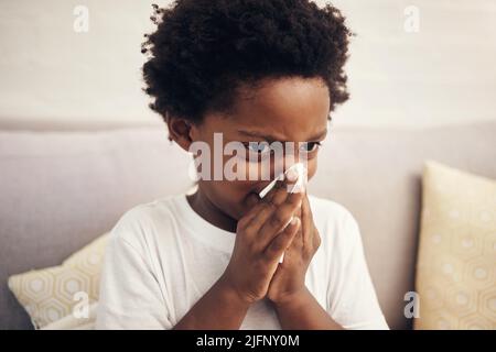 Erkältung und Grippesaison. Kranker afroamerikanischer Junge mit Afro, der Nase in das Gewebe bläst. Kind, das an einer laufenden Nase leidet oder niest und seine Nase bedeckt Stockfoto