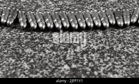 Viele Tokarev Pistolenkartuschen (7,62×25mm) liegen auf einem grauen Granit-Hintergrund, monochromes Foto Stockfoto