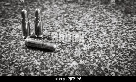 Drei Tokarev Pistolenkartuschen (TT) (7,62×25mm) auf grauem Granit-Hintergrund, monochromes Foto Stockfoto