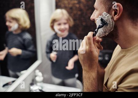 Nahaufnahme eines bärtigen Mannes, der sich im Badezimmer mit einem kleinen Jungen im Hintergrund rasieren konnte, Platz zum Kopieren Stockfoto