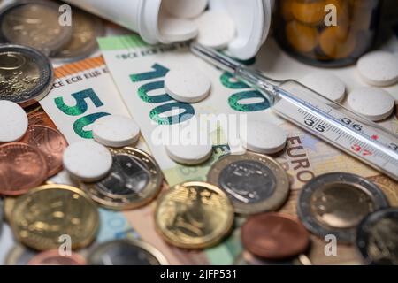 Pillen und Medizin mit klinischem Thermometer auf Geld. Euro in Banknoten und Münzen. 100-Euro-Rechnung im Fokus Stockfoto