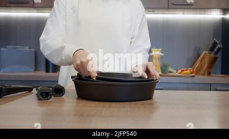 Nahaufnahme der Hände einer Frau, die neue Bratpfannen mit abnehmbarem Griff für die Küche vorführt. Aktion. Konzept der Hausgeräte. Stockfoto