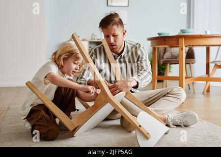 Ganzkörperportrait von Vater und Sohn, der in erdigen, gemütlichen Tönen Holzmöbel zusammenfügt Stockfoto