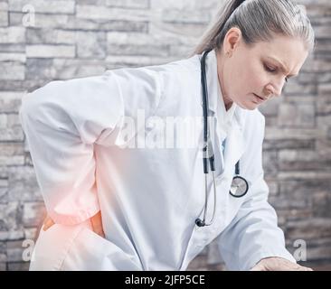 Meine Gesundheit ist nicht mehr das, was sie früher war. Aufnahme eines reiferen Arztes mit Schmerzen im unteren Rücken während der Arbeit in einer Arztpraxis. Stockfoto