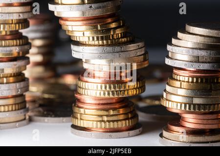 Aufgestapelte Münzen, Euro in verschiedenen Größen, die sich nach rechts auf weißer Oberfläche und dunklem Hintergrund lehnten Stockfoto