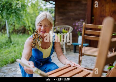 Ältere Frau putzt und renoviert Gartenmöbel und bereitet den Garten für den Sommer vor Stockfoto