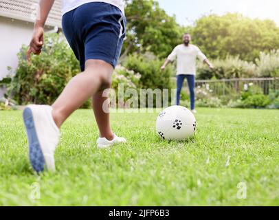 Ein Ziel erreichen. Nahaufnahme eines kleinen Jungen, der seinem Vater einen Fußballball abtritt, während er im Freien zusammen spielt. Stockfoto