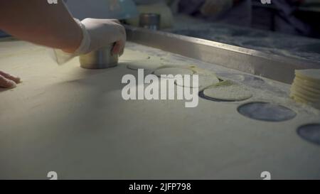 Nahaufnahme des Schneideteiges für Knödel. Clip. Cook macht schnell Knödelformen. Rundes Schneiden des Teigs für eine große Anzahl von Knödeln Stockfoto