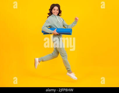 Sportbekleidung Werbekonzept. Laufen und springen. Teenager Kind Mädchen in Trainingsanzügen Jogginganzug posiert im Studio halten Fitness-Matte. Stockfoto