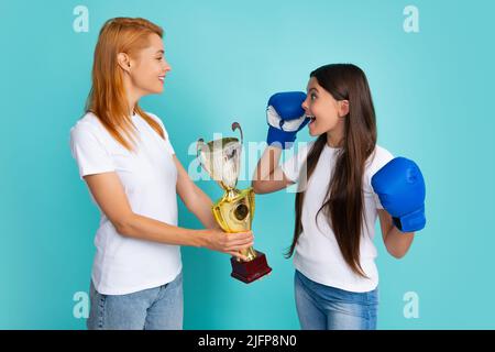 Mutter und Tochter im Teenageralter tragen Boxhandschuhe, emotional aufgeregt und glücklich. Frau und Mädchen feiern Erfolg, mit Triumph über blauen Hintergrund. Stockfoto