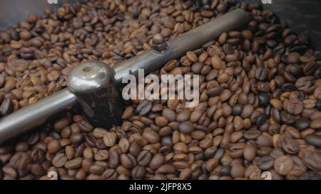 Röstung von Kaffeebohnen in der Fabrik. Aktion. Kaffeebohnen werden während des Röstens in der Industriemaschine gemischt. Industrielle Röstung von Kaffee in speziellen Stockfoto