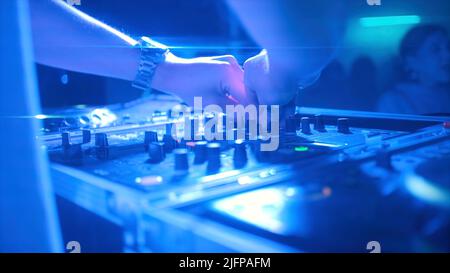 Frau arbeitet hinter Musikmixer. Clip. Junge Frau hinter DJ-Setup im Club. Coole weibliche DJ macht Musik in der Nachtdisco Stockfoto