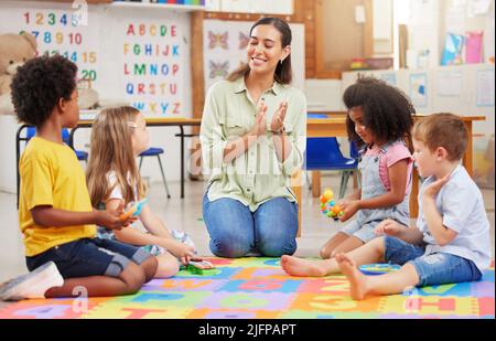 Wenn du glücklich bist und es weißt, klatsche in die Hände. Aufnahme einer Lehrerin, die mit ihren Vorschulkindern singt. Stockfoto