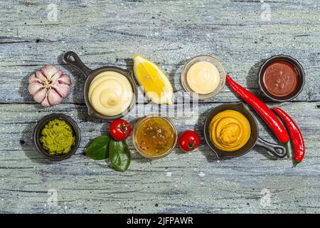 Set von Saucen und frischem Gemüse auf Holzhintergrund. Ketchup, Senf, Mayonnaise, Wasabi, süßes Und BBQ. Gewürze und Kräuter, trendige harte Lig Stockfoto