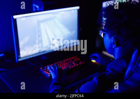 Über der Schulter Blick auf jungen schwarzen Mann spielen Videospiele im Cybersport-Club in blauen Neon-Beleuchtung Stockfoto