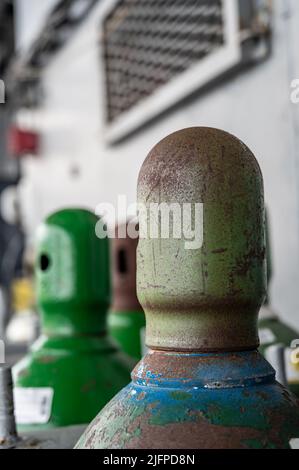 Druckgasflaschen, die vertikal durch eine Metallkette und eine Metallkappe gesichert gelagert werden. Stockfoto