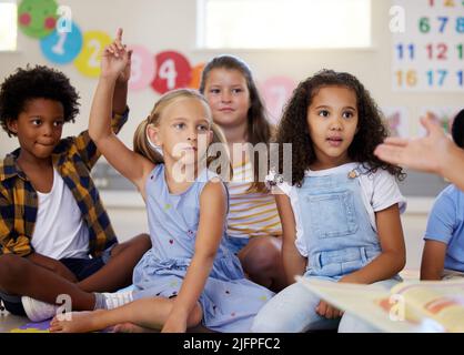 Wir lernen viel durch das Lesen. Aufnahme von kleinen Kindern, die in der Klasse die Hände heben. Stockfoto