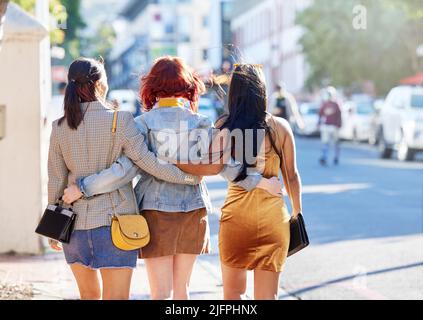 In die Stadt. Rückansicht von drei nicht erkennbaren jungen Freundinnen in der Stadt. Stockfoto