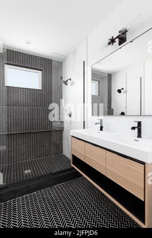 Ein wunderschön renoviertes Badezimmer mit einem Schrank aus Holz, schwarzen Marmorfliesen mit Fischgrätmuster in der Dusche und einer weißen Arbeitsfläche mit schwarzen Wasserhähnen. Stockfoto