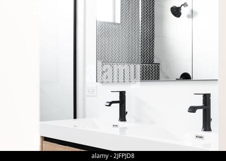 Ein wunderschön renoviertes Badezimmer mit einem Schrank aus Holz, schwarzen Marmorfliesen mit Fischgrätmuster in der Dusche und einer weißen Arbeitsfläche mit schwarzen Wasserhähnen. Stockfoto