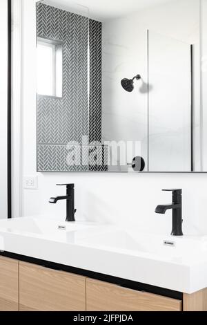 Ein wunderschön renoviertes Badezimmer mit einem Schrank aus Holz, schwarzen Marmorfliesen mit Fischgrätmuster in der Dusche und einer weißen Arbeitsfläche mit schwarzen Wasserhähnen. Stockfoto