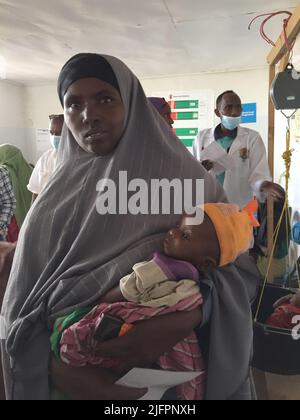 Baidoa, Somalia. 29.. Juni 2022. Nala Hassan hält ihren kleinen Sohn Rachid in den Armen. Die somalische Mutter ist mit dem stark unterernährten Baby in einer Klinik in Baidoa im Südwesten Somalias. Eine schwere Dürre hat eine Hungerkrise ausgelöst. Insbesondere die Zahl der lebensbedrohlichen unterernährten Säuglinge ist in den letzten Wochen stark gestiegen. (To dpa 'Wettlauf gegen die Zeit, um das Leben hungernder Kinder zu retten') Quelle: Eva-Maria Krafczyk/dpa/Alamy Live News Stockfoto